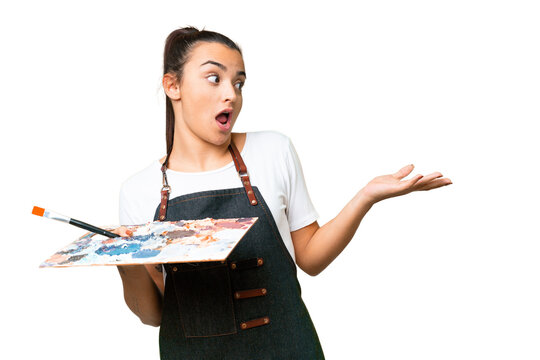 Young artist woman holding a palette over isolated chroma key background with surprise expression while looking side