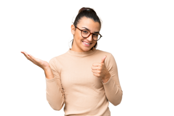 Young beauty woman over isolated chroma key background holding copyspace imaginary on the palm to insert an ad and with thumbs up