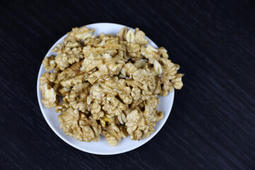 Peeled walnut kernels in a white plate on dark wooden table, top view. Protein food for brain health