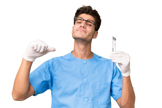 Young dentist man holding tools over isolated background proud and self-satisfied
