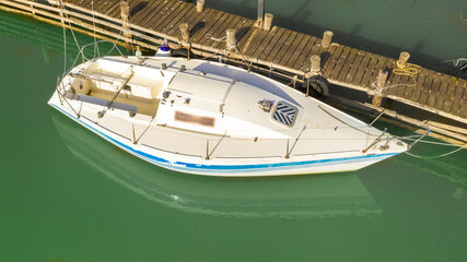 Aerial view of a small white motorboat anchored along a river jetty. The boat is white with blue decorations.