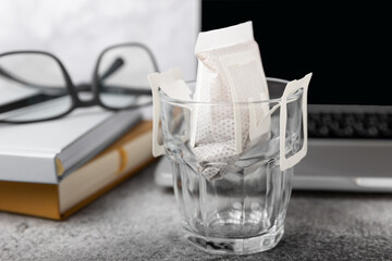 Drip coffee bags, coffee beans and a glass cup on a texture table. Ground coffee for brewing in a...