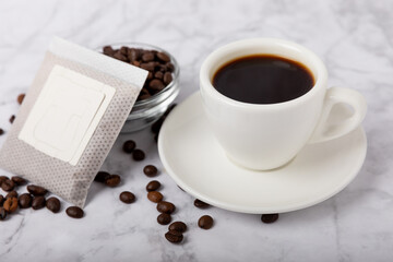 Drip coffee bags, coffee beans and a white cup on a texture table. Ground coffee for brewing in a cup, paper bag drip coffee filter packaging. Place to copy. Place for text.