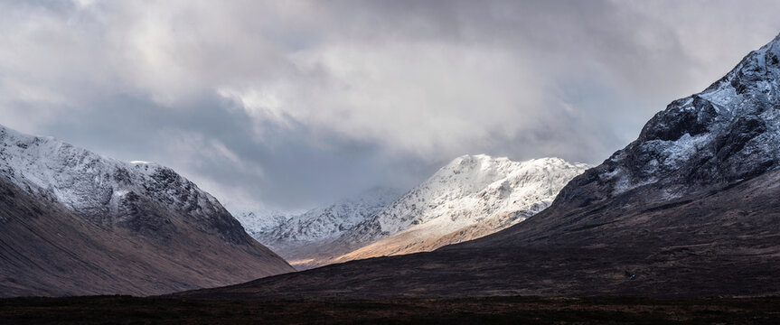 Majestic beautiful Winter landscape image of Lost Valley in Scotland with snowcapped Buachaile Etive Baeg sand distant mountain range with dramatic sky