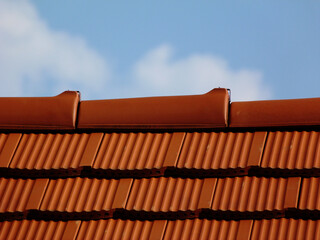 brand new sloped clay roof ridge detail. bright red clay roofing. clear blue sky and beautiful light fluffy white clouds in bright sunlight. construction industry and building renovation concept