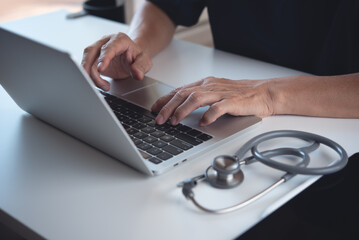 Close up of doctor working on laptop computer and using digital tablet on table in doctor's office,...