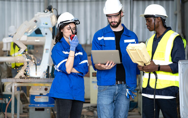Industrial engineer using laptop computer to control robotic welder arm operation in modern automation factory. Technician monitoring robot machine arm does automated steel welding full of fire sparks