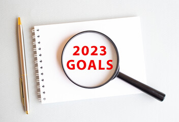The magnifying glass rests on the pad and shows 2023 GOALS on a white page. There is a pen next to it.