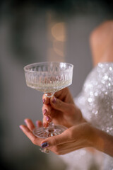 The hands of a woman hold a glass of champagne on a background of golden beke. The concept of the holiday, Christmas, new year, birthday.