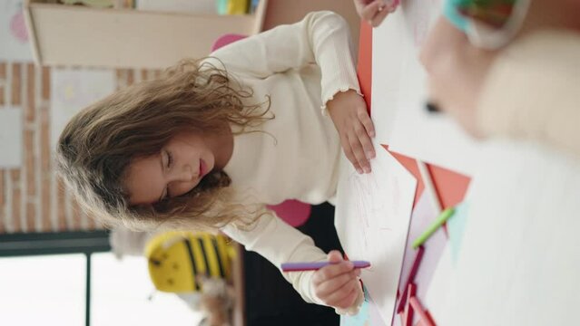 Adorable caucasian girl student sitting on table drawing on paper at classroom