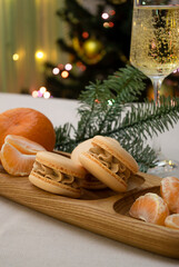 Macaron cookies with mandarin ganache and mandarins on the plate. Dessert with christmas lights and decoration