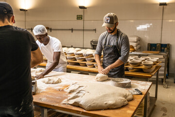 Caucasian master baker teaching the kneading technique to his African apprentice in the bread...
