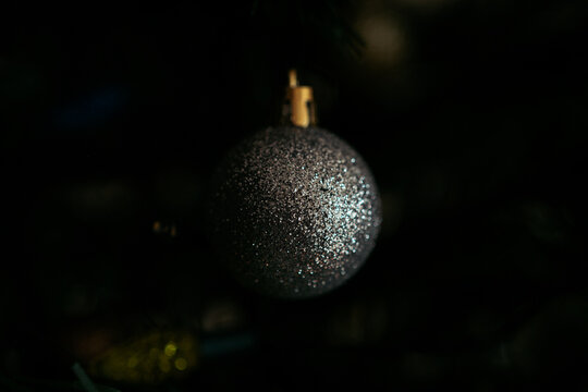 Moody image of sparkling silver Christmas tree ball ornament with glitter on dark background, selective focus macro shot for holiday or christmas card