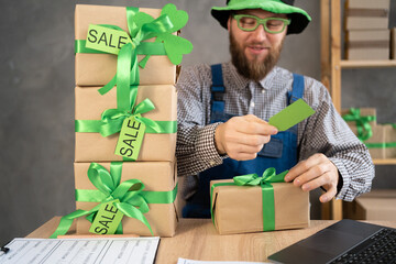 Small business owner with laptop and gift boxes with sale tags on table in home warehouse. Online ecommerce retail business St.Patricks Day discounts deals, free shipping.