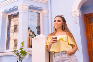 Portrait of young blonde in a neighborhood with houses with colorful facades, with a cafe in her home