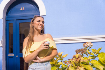Portrait of blonde woman in houses with blue colorful facades, with a cafe at the door of her house