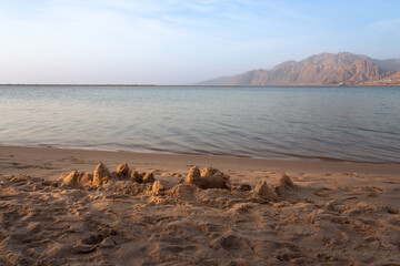 Fototapeta na wymiar Remains of sand castle on sandy beach lit by early sunlight with mountains in background Dahab Egypt
