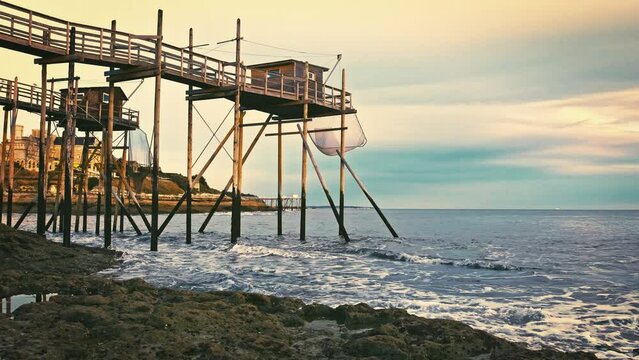 Rocky sea coast beach of Saint Palais in France with fishing hut and nets in sunset time. Ocean coast with constraction for fish catching and evening orange sky