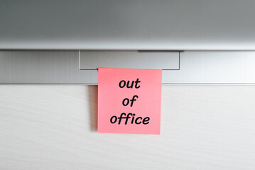 Memo sticker with message Out of office stuck on closed laptop at workplace, close-up. Concept of...