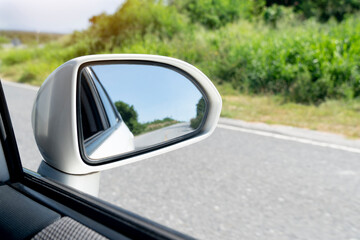 Mirror view of white car travel on the asphalt road. with blurred of green grass at day.