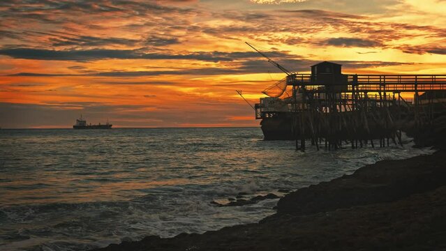 Rocky sea coast beach of Saint Palais in France with fishing hut and nets in sunset time. Ocean coast with constraction for fish catching and evening orange sky