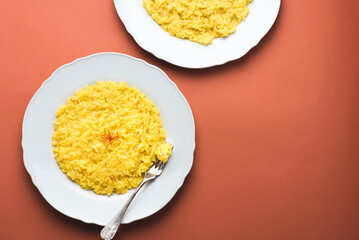 Risotto alla Milanese in a white aristocratic dish on the red terracotta background. A classic recipe for Lombard risotto with saffron for the cold season. Cuisine of the north Italy , close-up