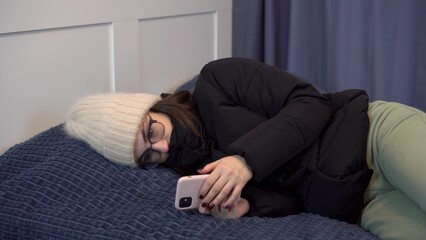 A young girl in a jacket warms herself on the bed and uses the phone. A woman in a jacket freezes...
