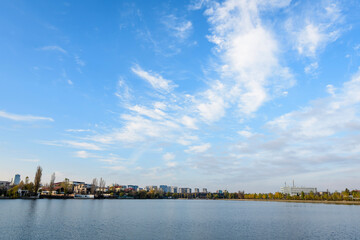 Landscape with trees and the lake in Linden Park (Parcul Tei), in Bucharest, Romania, in a sunny autumn day with white clouds and blue sky