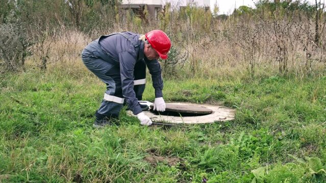 a male plumber in overalls opens the manhole of a water well with a crowbar. Inspection of water meter readings.
