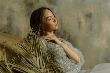 a girl in a dress on the sand against a shabby wall with dry grass