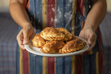 Woman in an apron stained with flour holding a tray with Argentine empanadas.