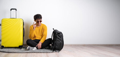 Full height traveler tourist man in sweater with suitcase sit, pointing finger up with successful idea isolated on white background Passenger travel abroad weekends getaway. Air flight journey