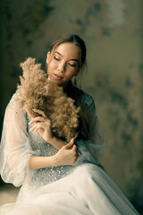 a girl in a dress with dry grass on the background of a shabby wall