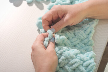 woman knitting with fingers turquoise plaid. Finger Knit a Chunky Yarn Blanket. hands of knitting woman. copy space.