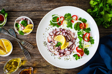 Octopus carpaccio with lemon and greens on wooden table
