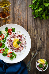 Octopus carpaccio with lemon and greens on wooden table

