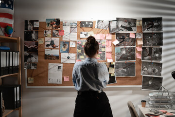 Young female detective looking at evidence board, back view.