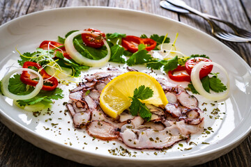 Octopus carpaccio with lemon and greens on wooden table

