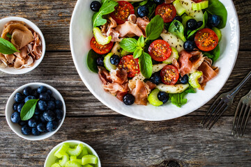 Fresh salad - prosciutto Crudo, pear, tomatoes and leafy vegetables on wooden table
