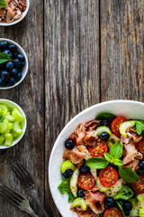 Fresh salad - prosciutto Crudo, pear, tomatoes and leafy vegetables on wooden table
