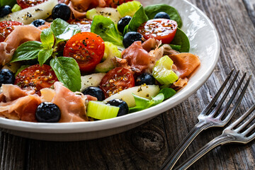 Fresh salad - prosciutto Crudo, pear, tomatoes and leafy vegetables on wooden table
