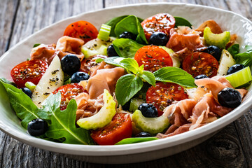 Fresh salad - prosciutto Crudo, pear, tomatoes and leafy vegetables on wooden table
