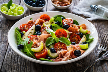Fresh salad - prosciutto Crudo, pear, tomatoes and leafy vegetables on wooden table
