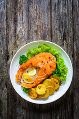 Fried salmon steak with potatoes and fresh vegetable salad served on wooden table
