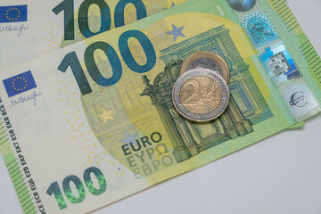 Two Euros coin and One Euro coin on top of One Hundred Euros Banknotes on a table. Copy space