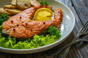 Fried salmon steak with potatoes and fresh vegetable salad served on wooden table
