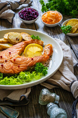 Fried salmon steak with potatoes and fresh vegetable salad served on wooden table
