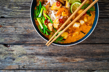 Tom Yum - Thai soup with halibut nuggets and rice noodles on wooden table
