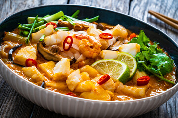Tom Yum - Thai soup with halibut nuggets and rice noodles on wooden table
