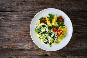 Fried calamari rings with lemon, greens and cherry tomatoes on wooden table
